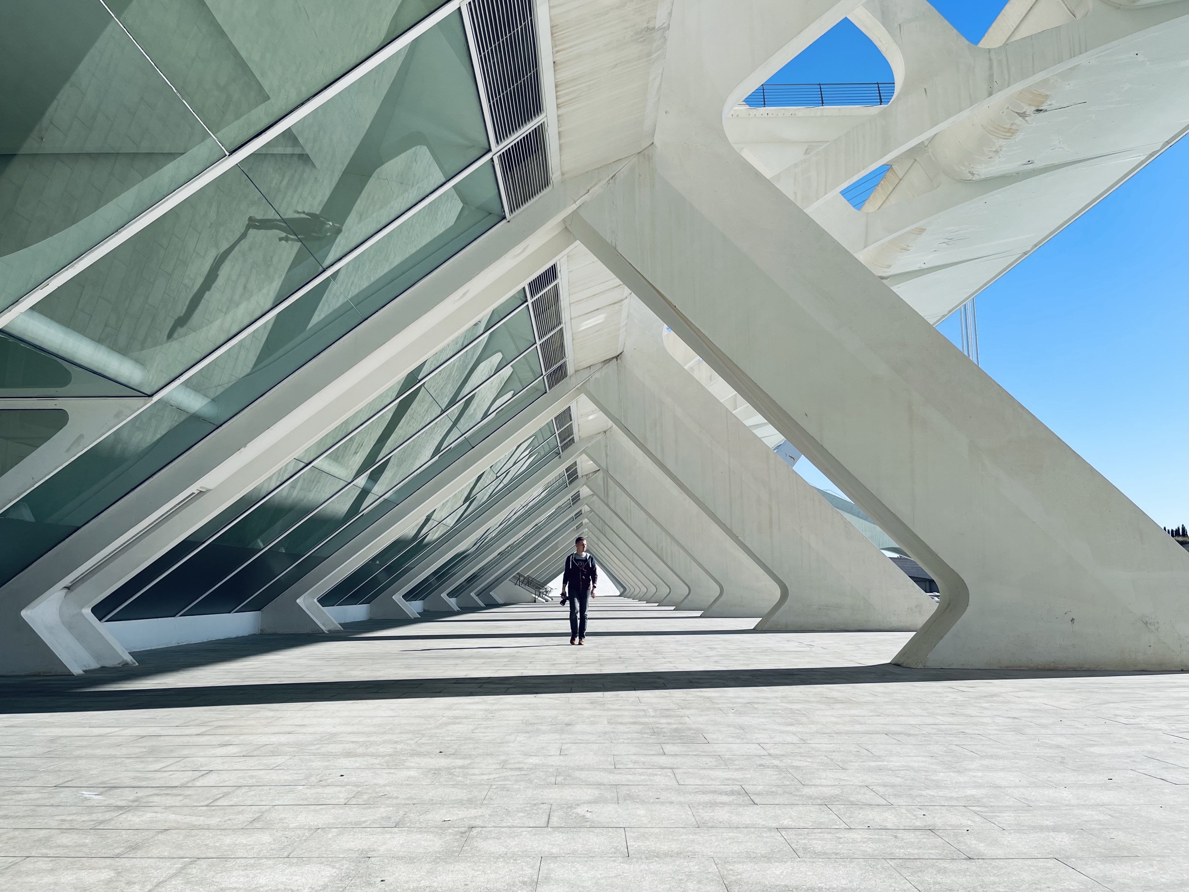 A solitary operator walking through a modern architectural colonnade — disciplined execution inside a well-designed system.