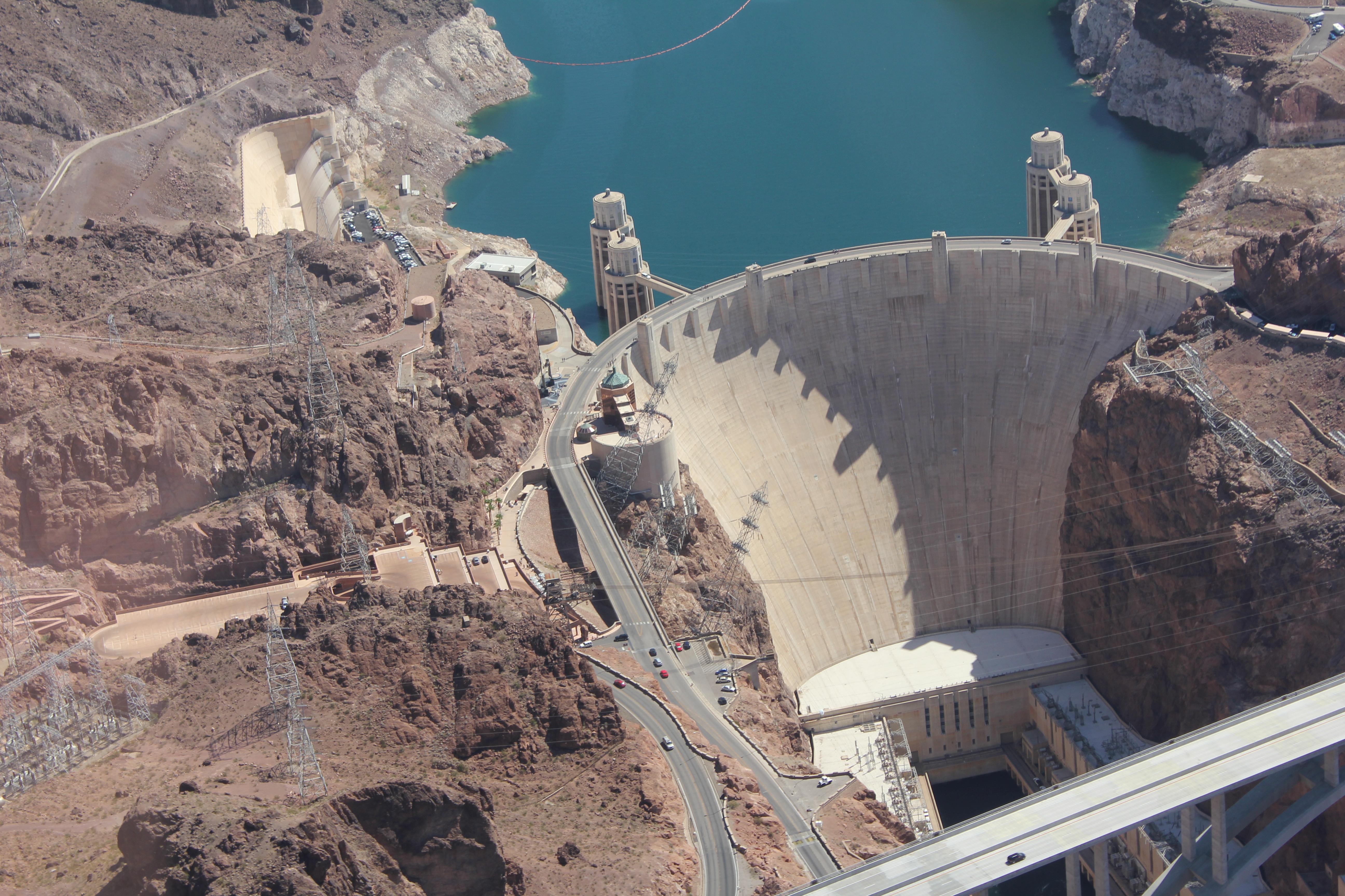 Aerial view of a precision-engineered dam holding back a deep blue reservoir — capital, infrastructure, and flow systems operating in concert.