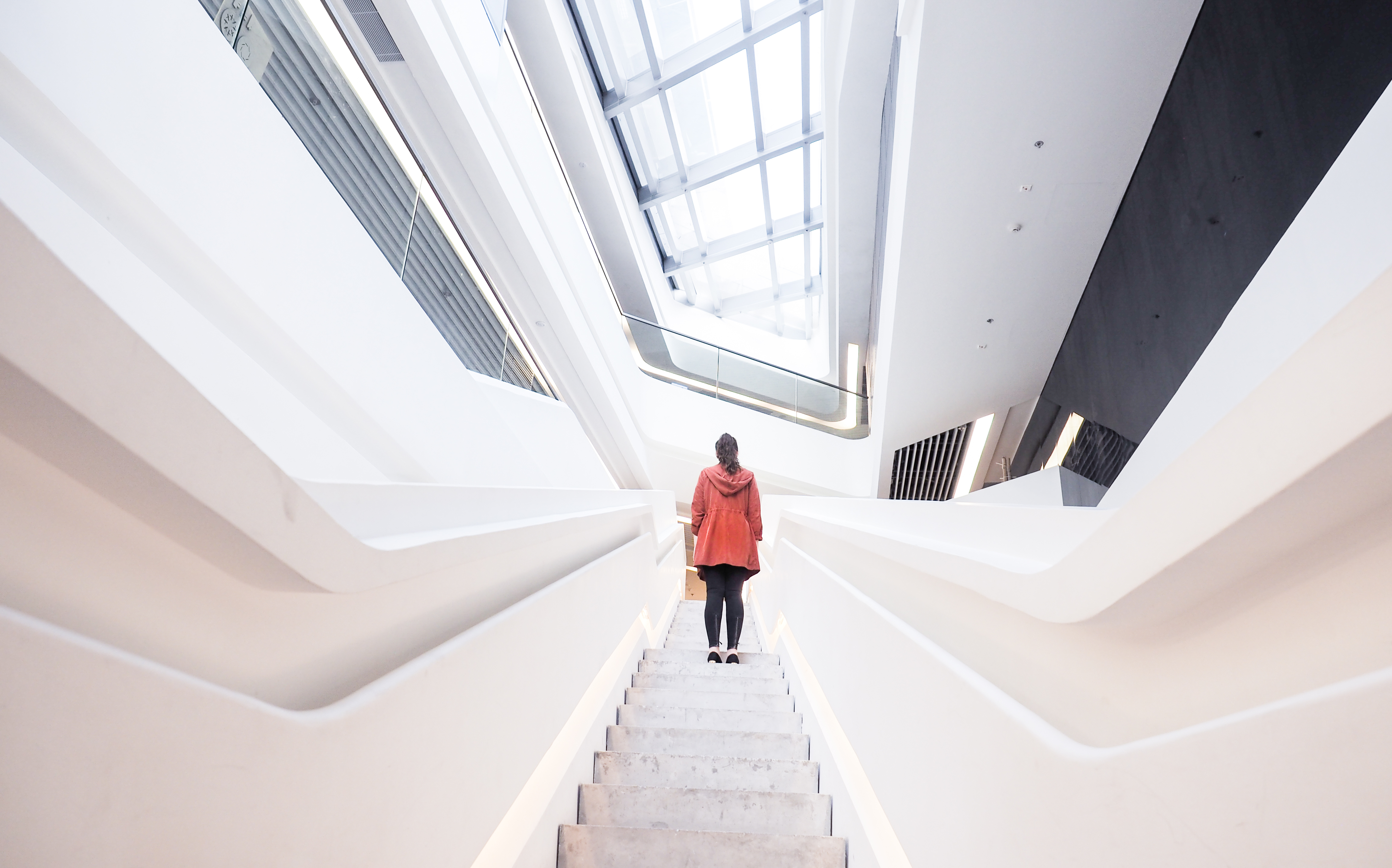A figure in motion ascending a sculptural white staircase — leadership rising through a system designed for clarity.